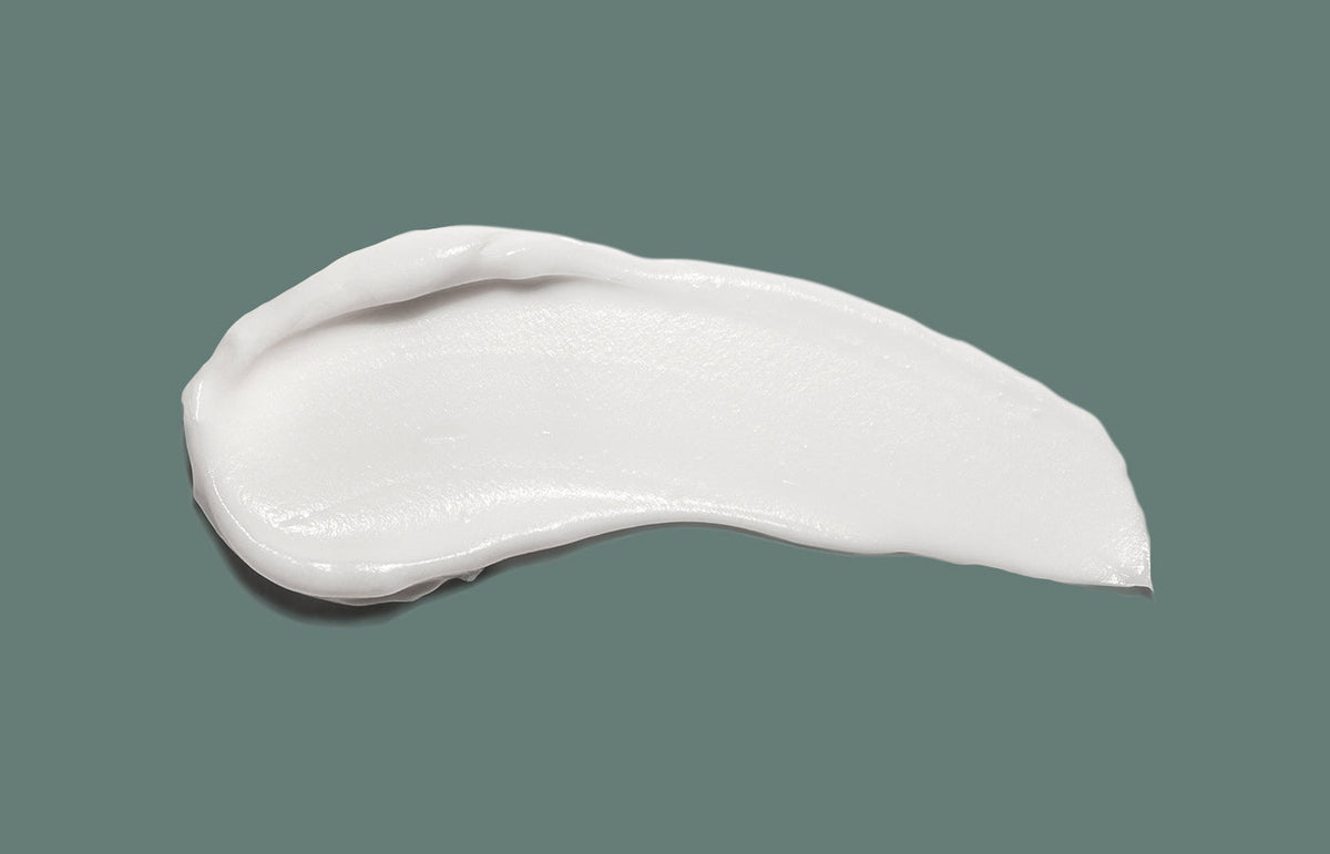 Swatch of white hand cream smeared across a sage green background