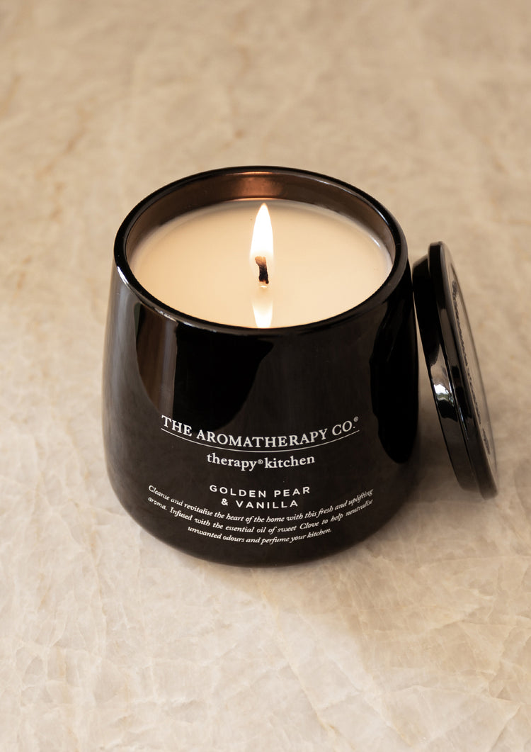 Lit Therapy Kitchen candle with its lid resting beside it on pale stone