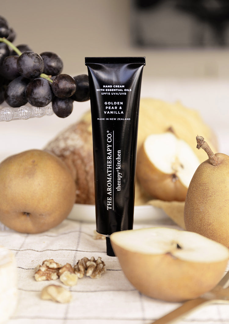 Hand cream tube standing on a check cloth in front of pears, a loaf and a bunch of black grapes
