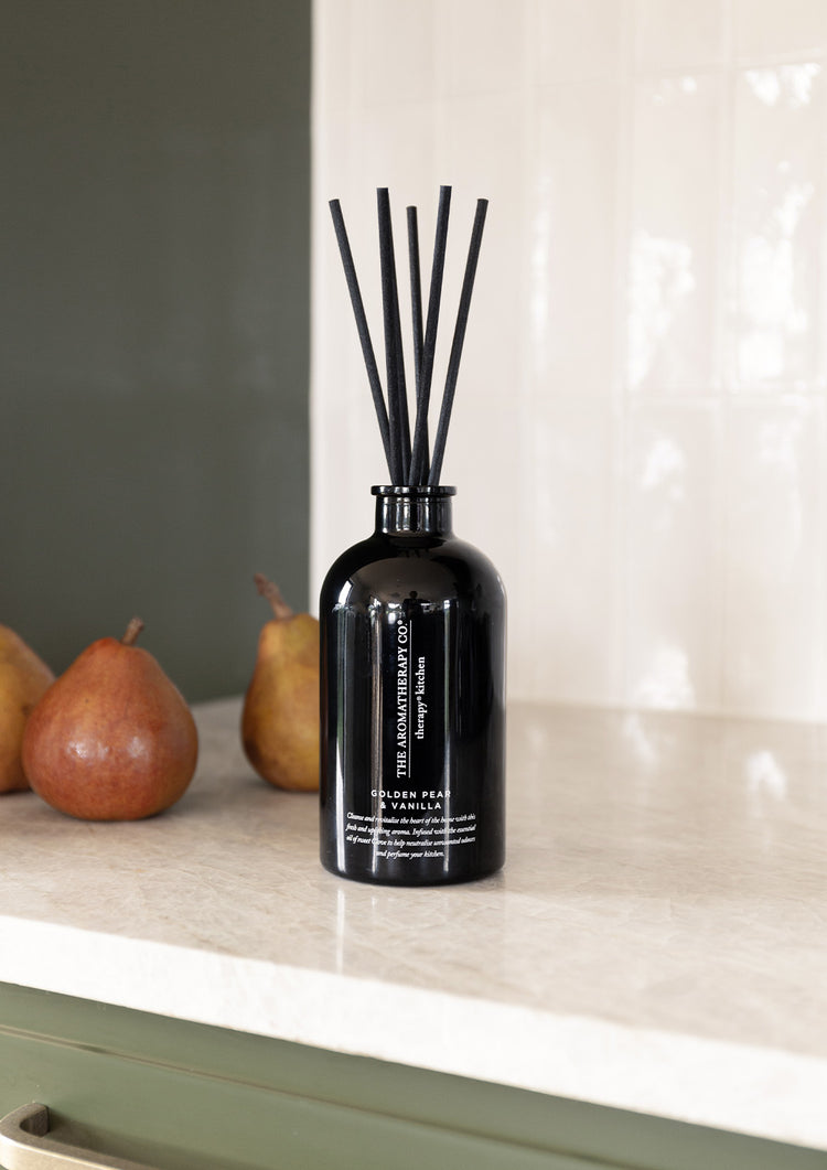 Black Therapy Kitchen reed diffuser beside two pears on a stone kitchen bench
