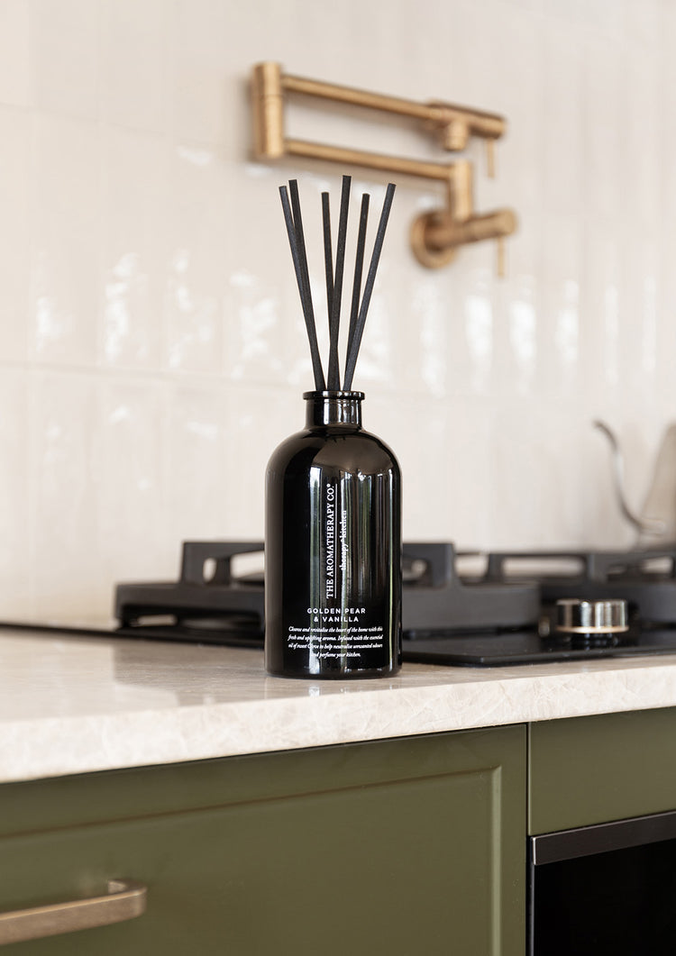 Black reed diffuser on a marble kitchen bench below a brass pot filler tap