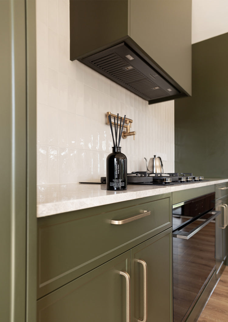 Olive green kitchen with a rangehood, cooktop and a black reed diffuser on the bench