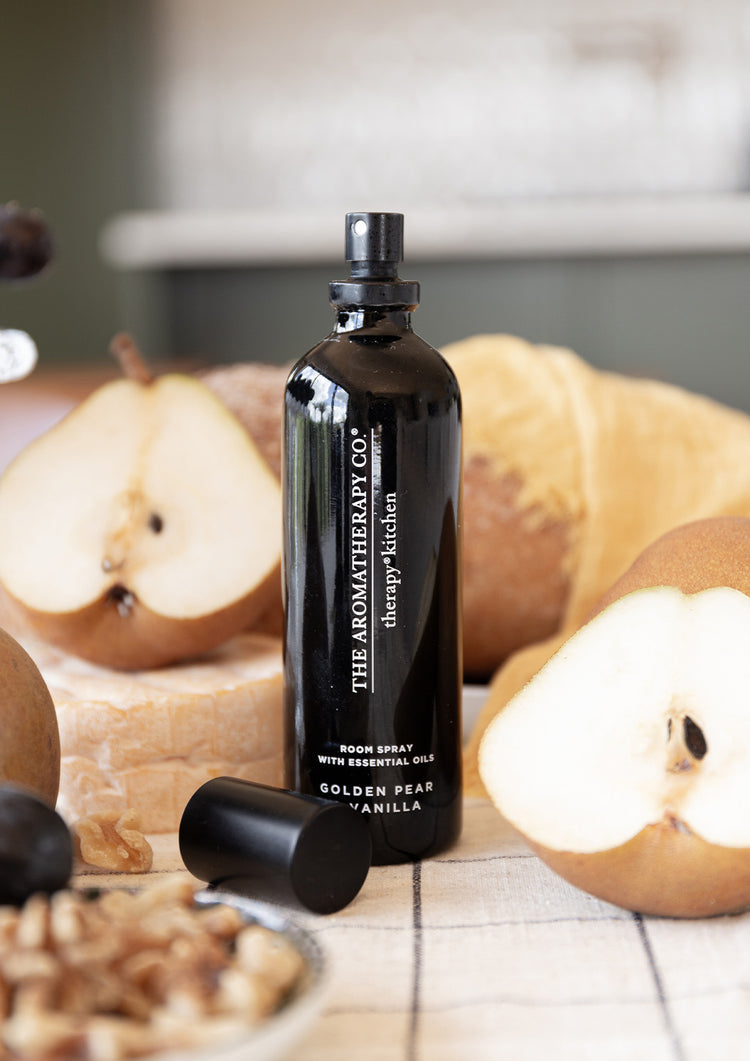 Golden Pear & Vanilla room spray with its cap off among halved pears, bread and walnuts