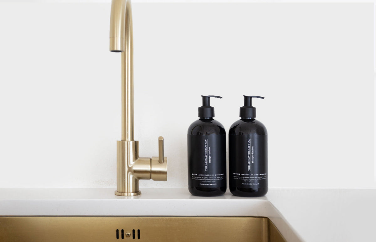 Two black pump bottles beside a brass tap on a white kitchen bench, landscape view