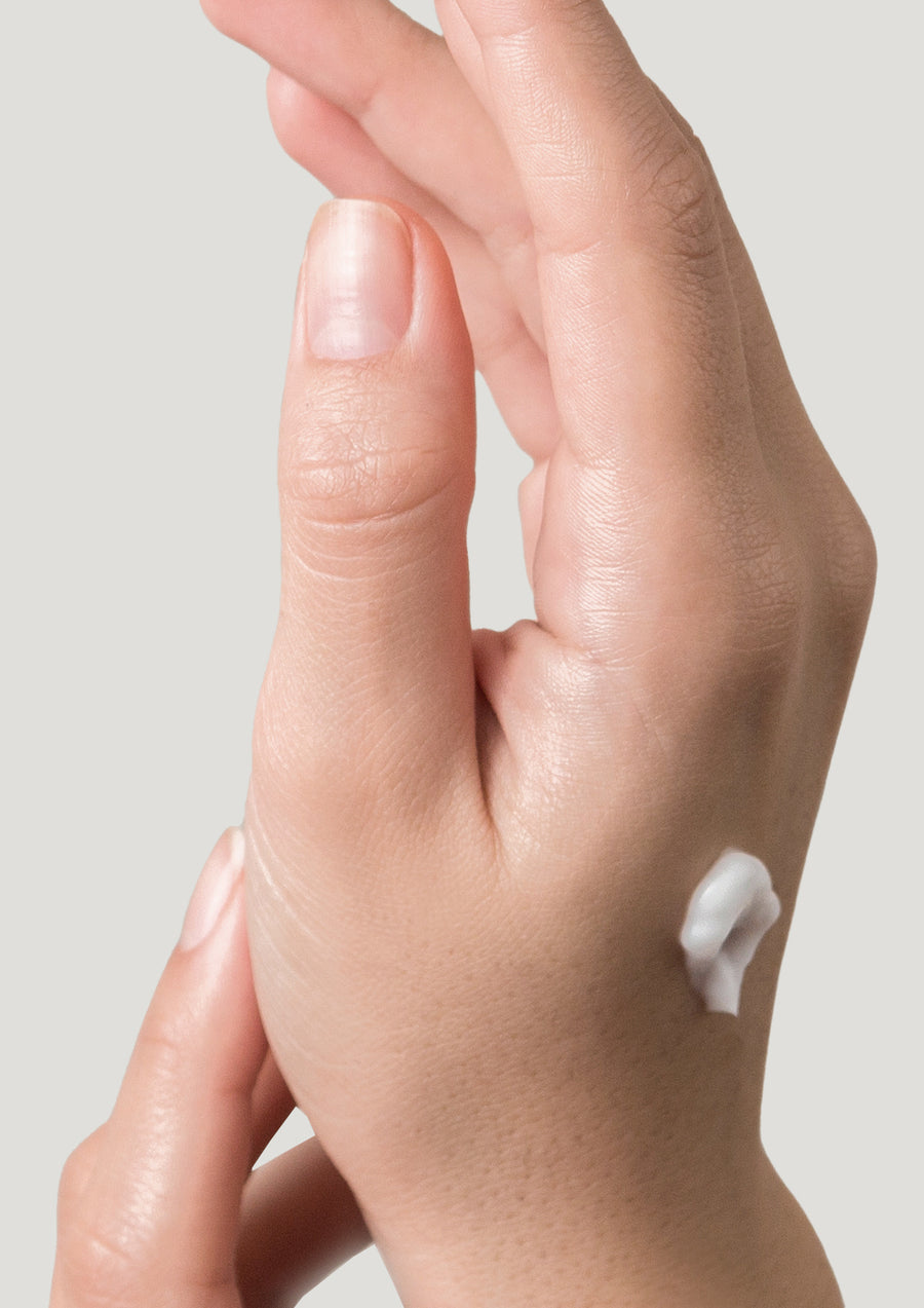 Hand with a dab of white hand cream on the back against a pale grey background
