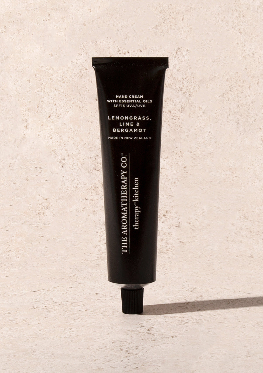 Black Therapy Kitchen hand cream tube standing on pale sandstone with a hard shadow