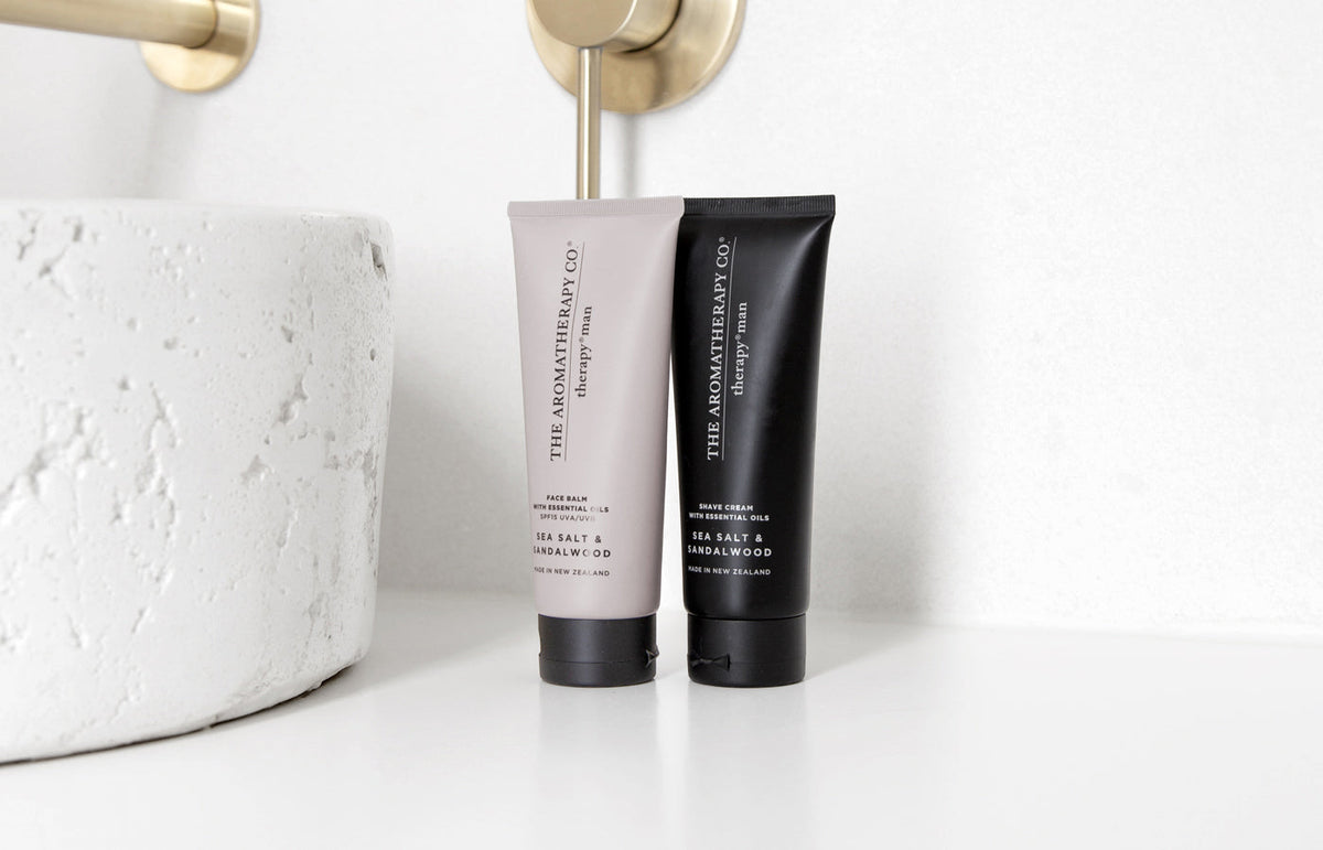 Grey face balm tube and a black Therapy Man tube beside a stone basin and brass tap, landscape view