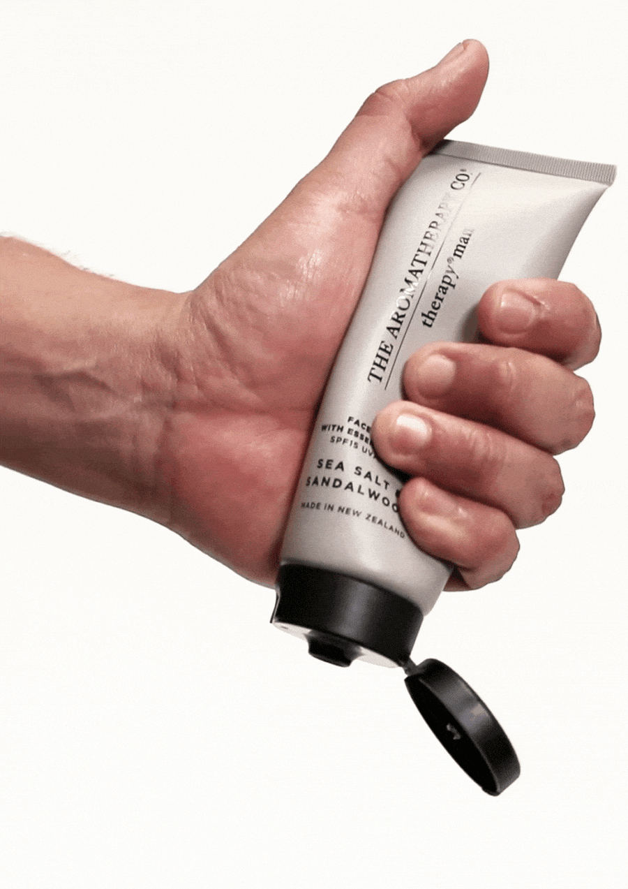 Hand squeezing the open Sea Salt & Sandalwood face balm tube against white