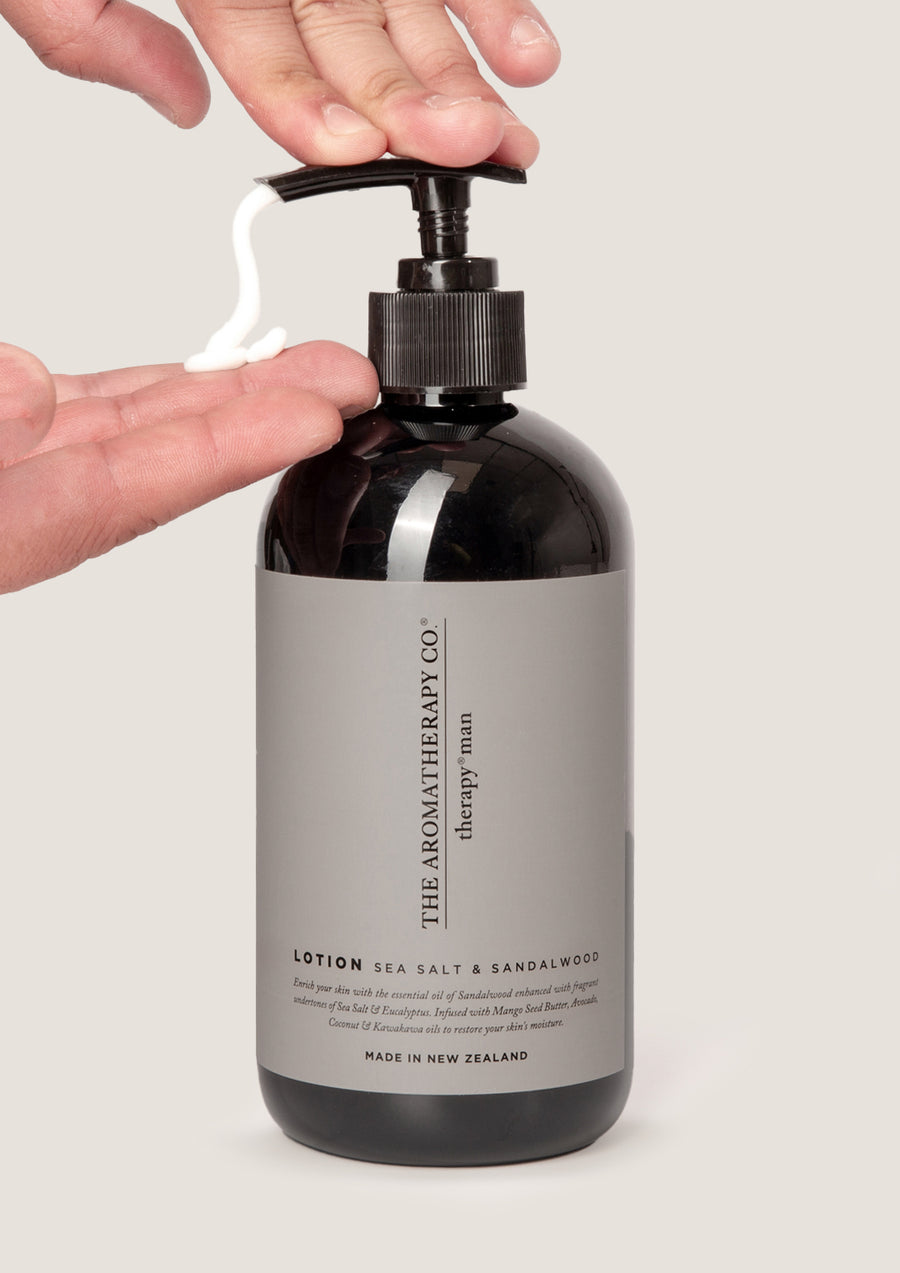 Hand pumping lotion from the Therapy Man Sea Salt & Sandalwood bottle against pale grey