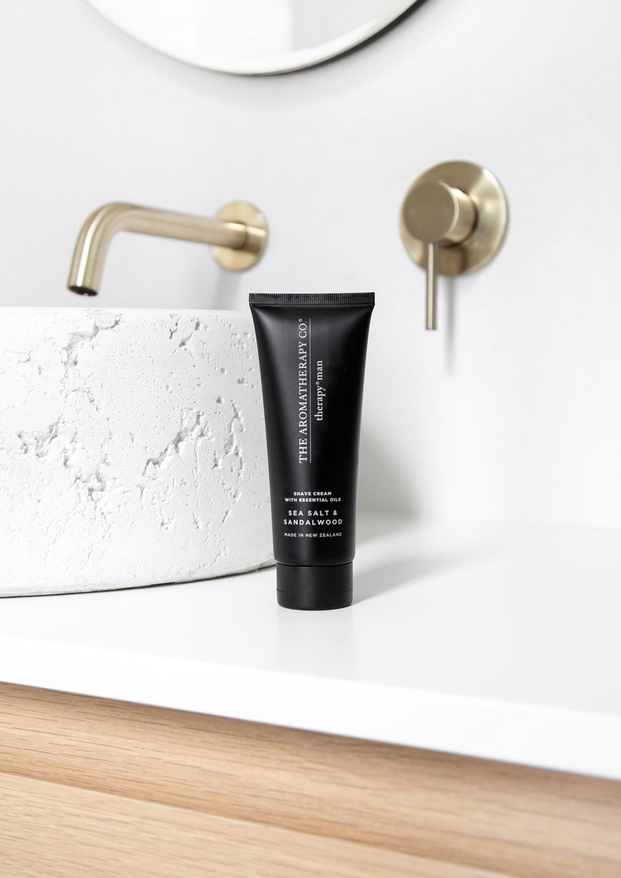 Black Therapy Man shave cream tube on a white vanity beside a stone basin and brass tap