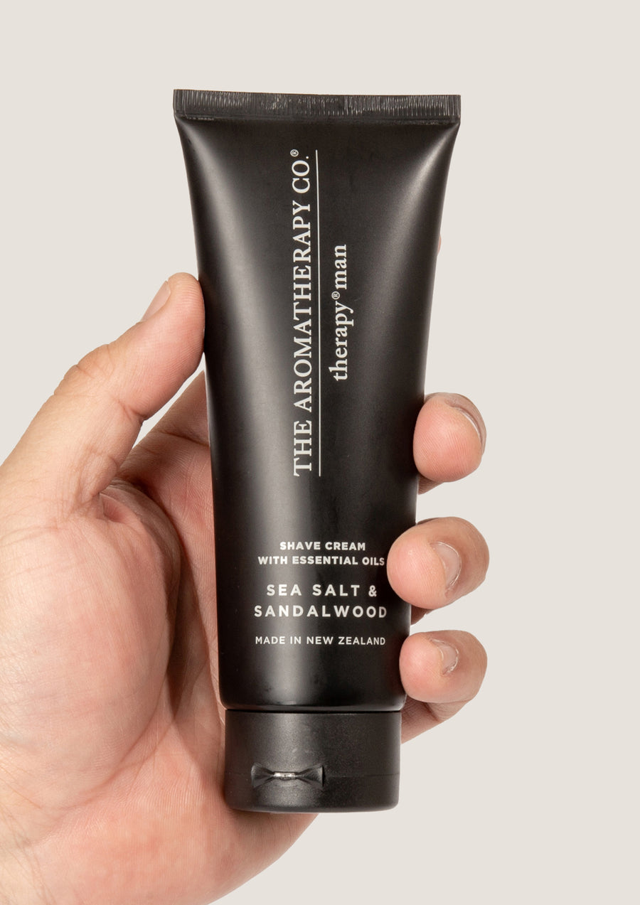 Hand holding the black Therapy Man Sea Salt & Sandalwood shave cream tube against pale grey