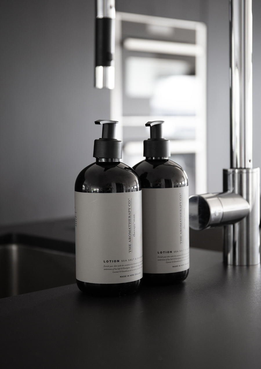 Therapy Man lotion and wash pump bottles beside a steel mixer tap on a dark kitchen bench