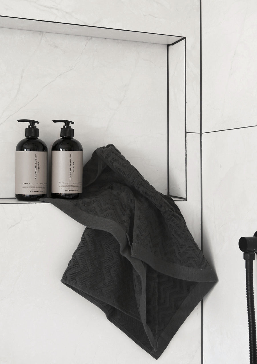 Two dark Therapy Man pump bottles in a white shower niche with a charcoal face cloth draped below