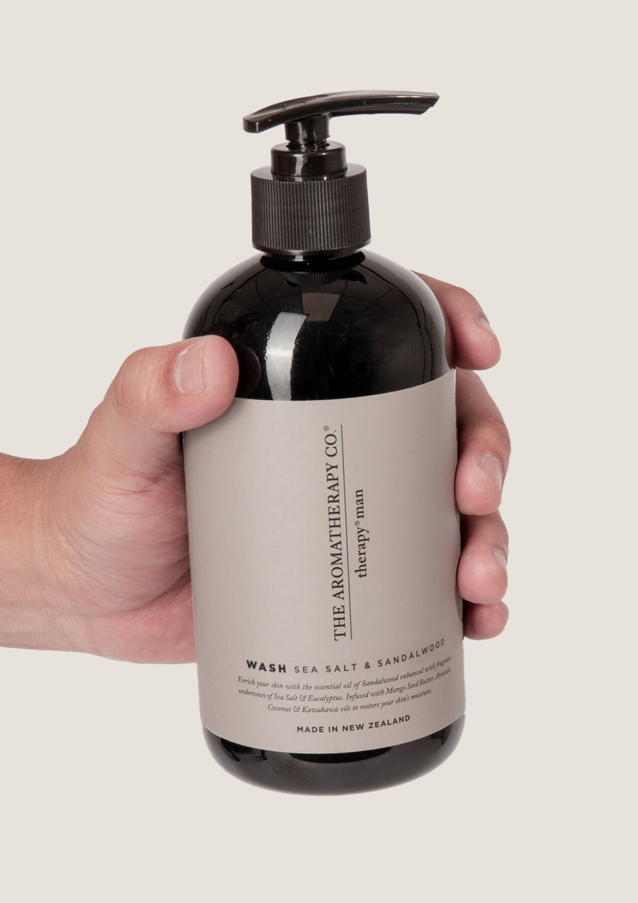 Hand holding the Therapy Man Sea Salt & Sandalwood wash bottle against a pale grey background