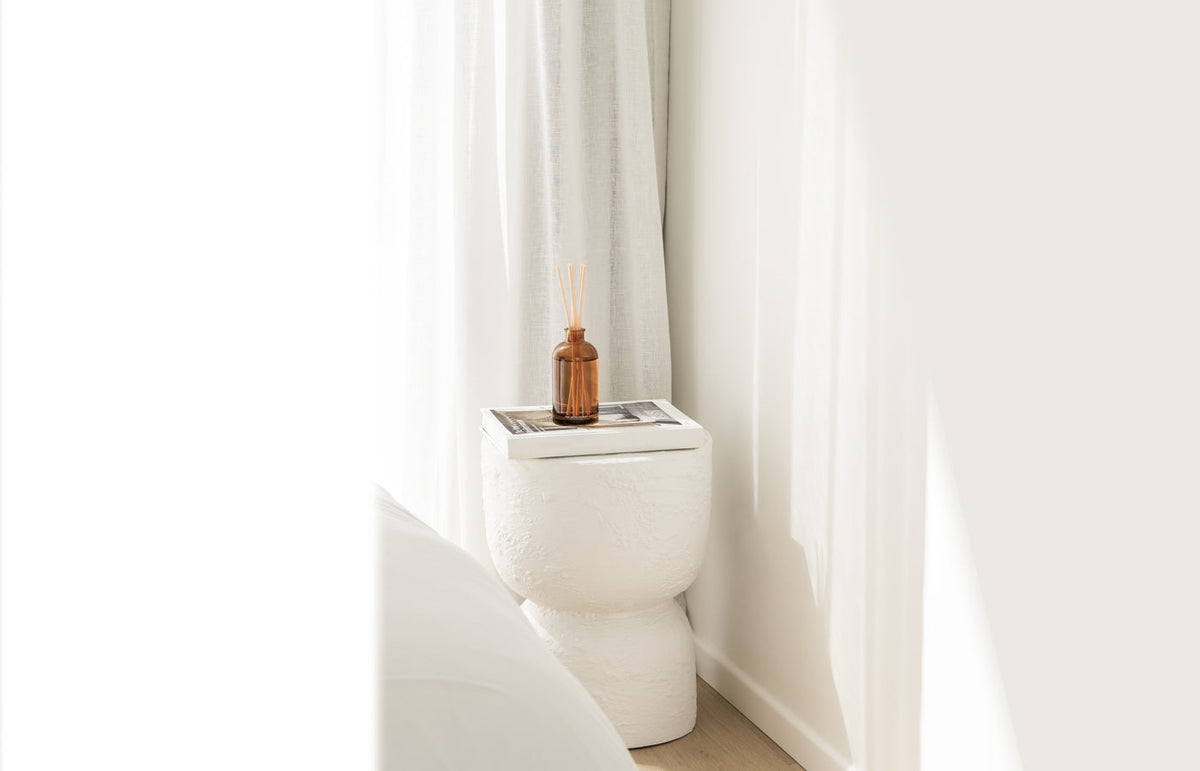 Therapy amber reed diffuser on a white cabinet beside sheer curtains, landscape view