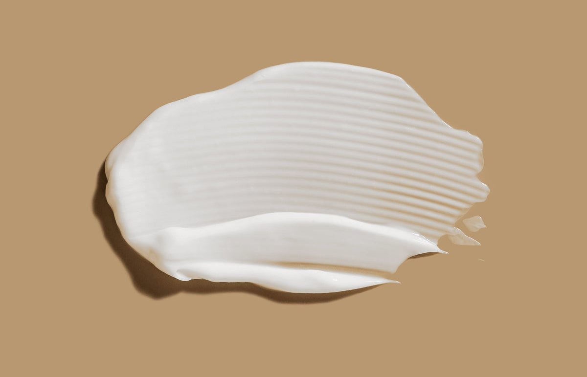 Swatch of white lotion smeared across a caramel background