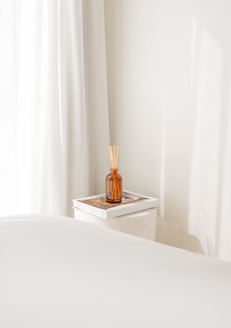 Bedroom with the Therapy amber reed diffuser on a white bedside beside sheer curtains
