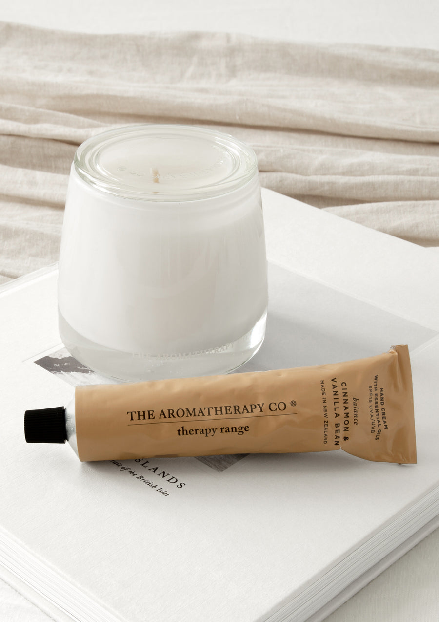 Caramel hand cream tube lying on an open book beside a white glass candle on linen