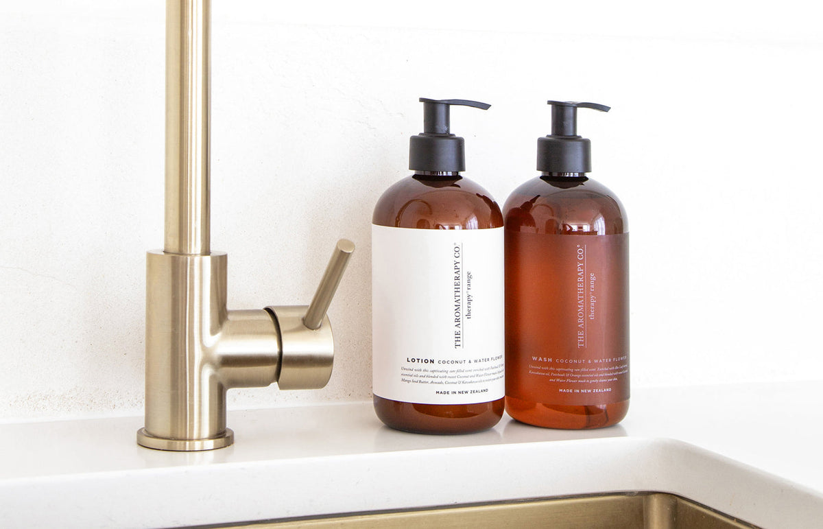 Therapy lotion and wash bottles beside a brass mixer on a white kitchen bench, landscape view
