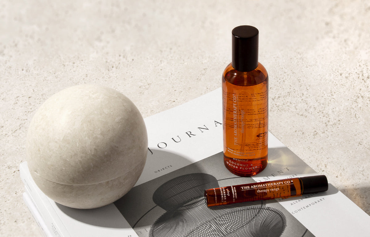 Amber room spray and a matching rollerball on an open journal beside a stone sphere