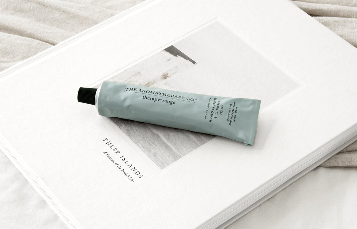 Sage blue hand cream tube on an open book on white linen, landscape view