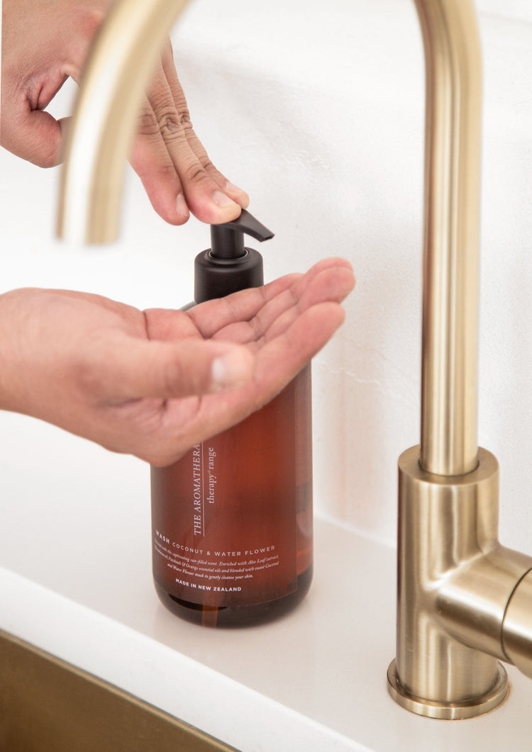 Hand pumping wash from an amber Therapy bottle beside a brass gooseneck tap and brass sink