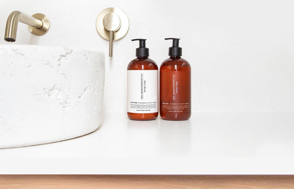 Two Therapy pump bottles beside a stone basin and brass tap on a white vanity, landscape view
