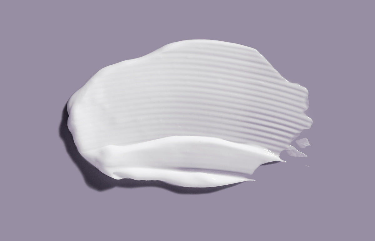 Swatch of white lotion smeared across a lilac grey background