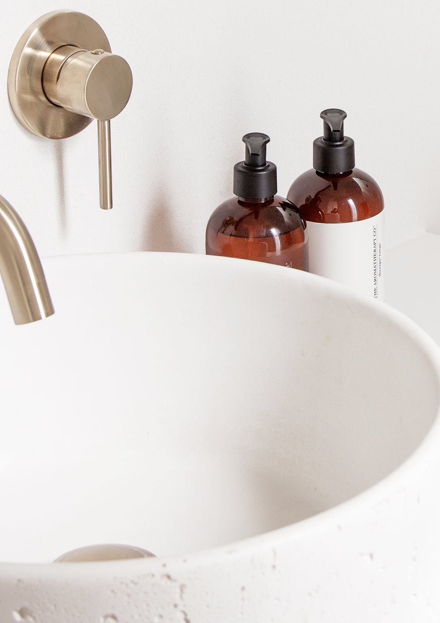 Close crop of two amber pump bottles behind the rim of a white stone basin with a brass mixer