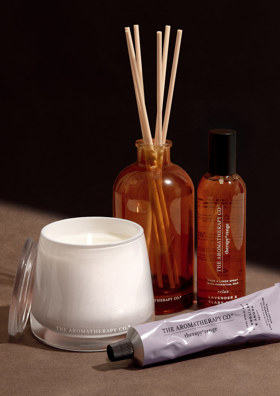Therapy candle, reed diffuser, room spray and lilac hand cream on a dark timber surface