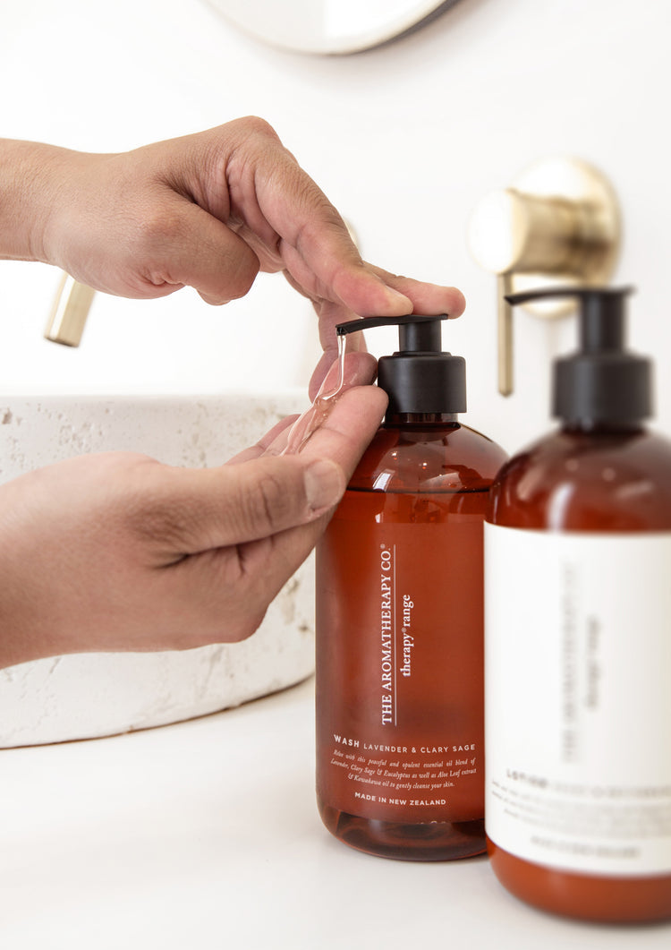 Hand pumping wash from an amber Therapy bottle beside a lotion bottle at a stone basin