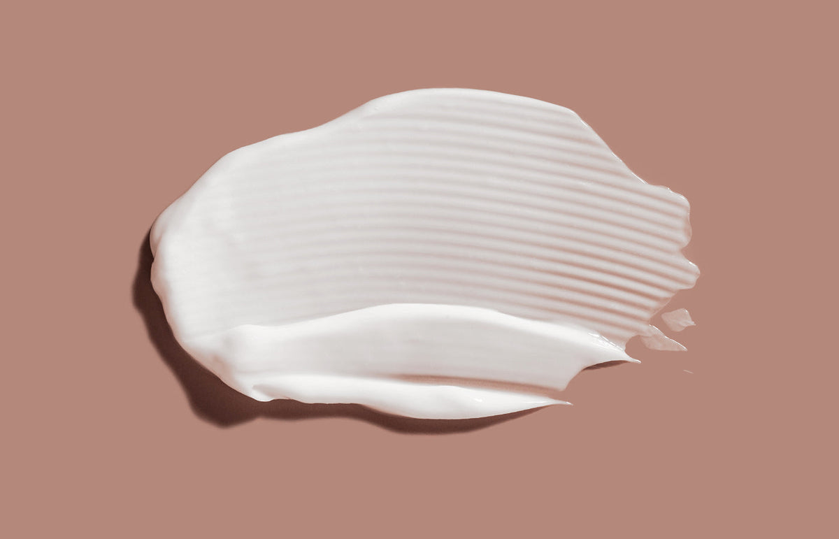 Swatch of white lotion smeared across a dusty pink background