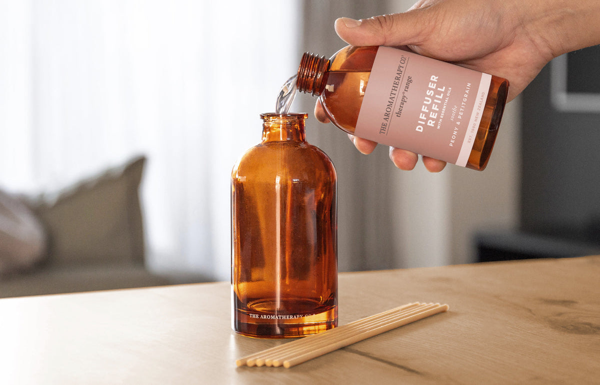 Hand pouring refill oil into an amber Therapy diffuser bottle