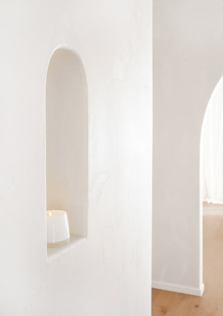 Small white candle tucked into an arched plaster wall niche in a white hallway