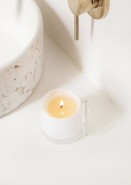 Close view of a lit white candle on a white vanity below a brass wall spout