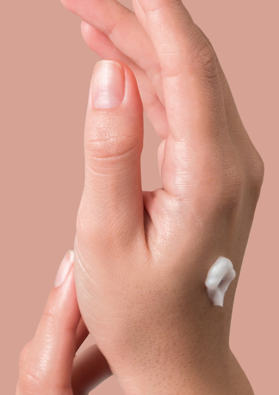 Hand with a dab of white hand cream on the back against a dusty pink background