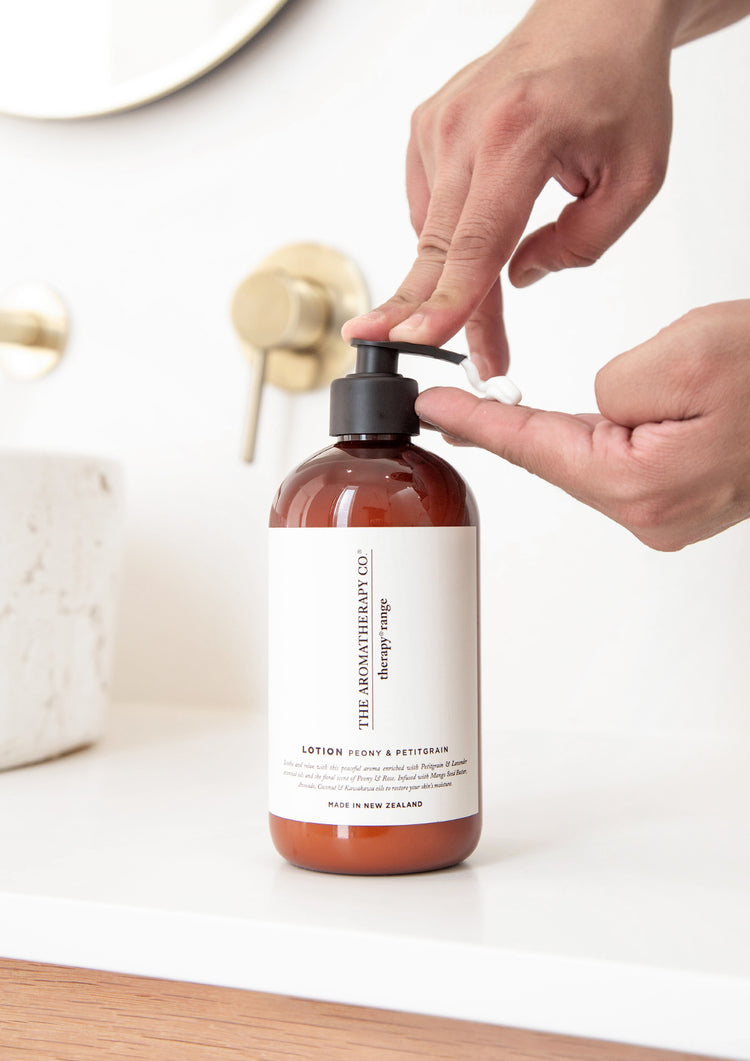 Hand pumping the Peony & Petitgrain lotion onto fingers beside a brass tap and stone basin