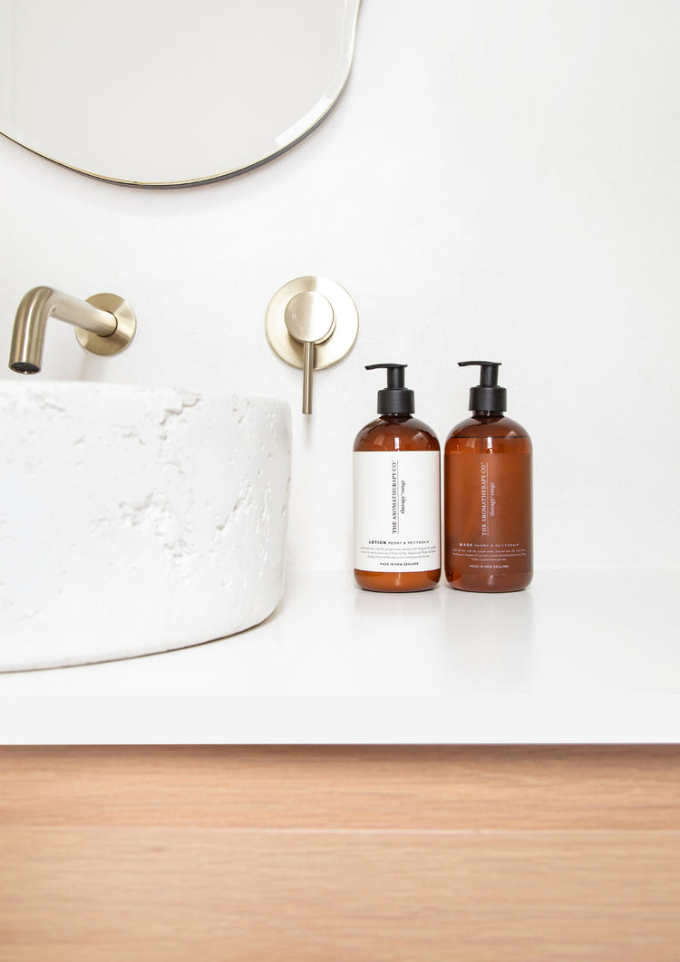 Two amber Therapy pump bottles on a white vanity beside a stone basin and brass wall tap
