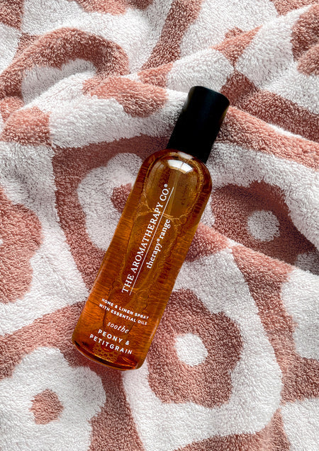 Peony & Petitgrain room spray lying on a rust and white patterned towel
