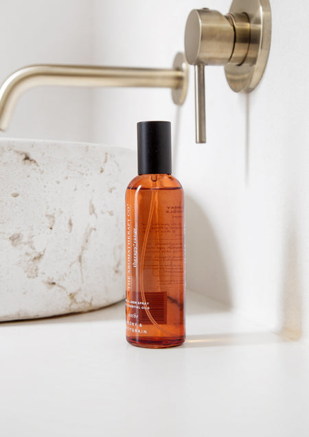 Amber room spray on a white vanity beside a stone basin and brushed brass tap