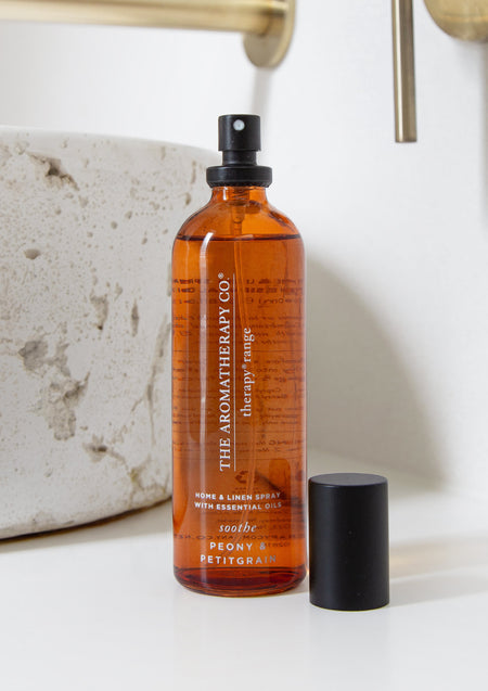 Close view of the Soothe Peony & Petitgrain spray with its cap off beside a stone basin