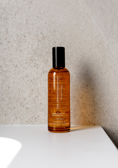 Amber Embrace room spray on a curved white ledge against a speckled stone wall