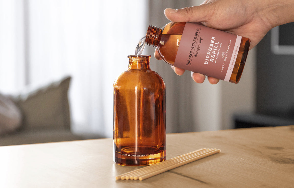 Hand pouring refill oil into an amber Therapy diffuser bottle