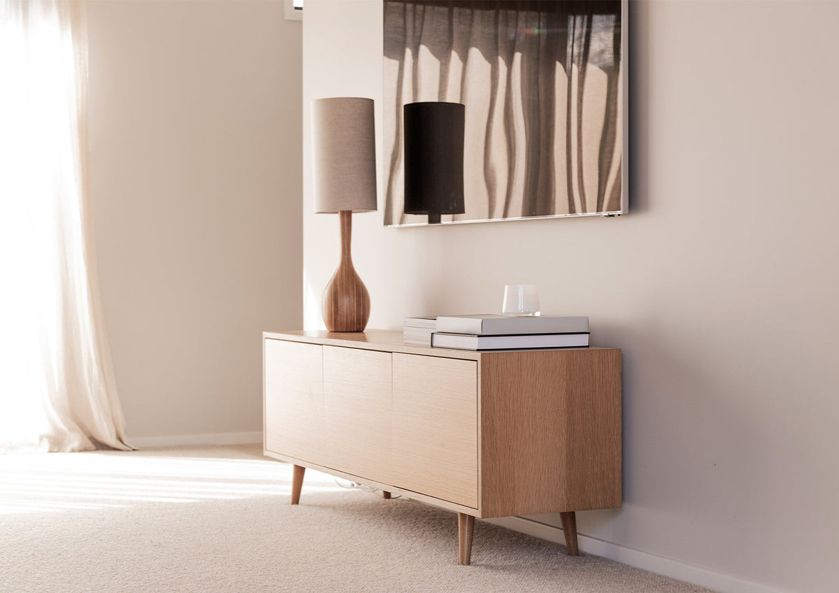 Pale oak sideboard with a lamp, books and a small candle in a sunlit room, landscape view