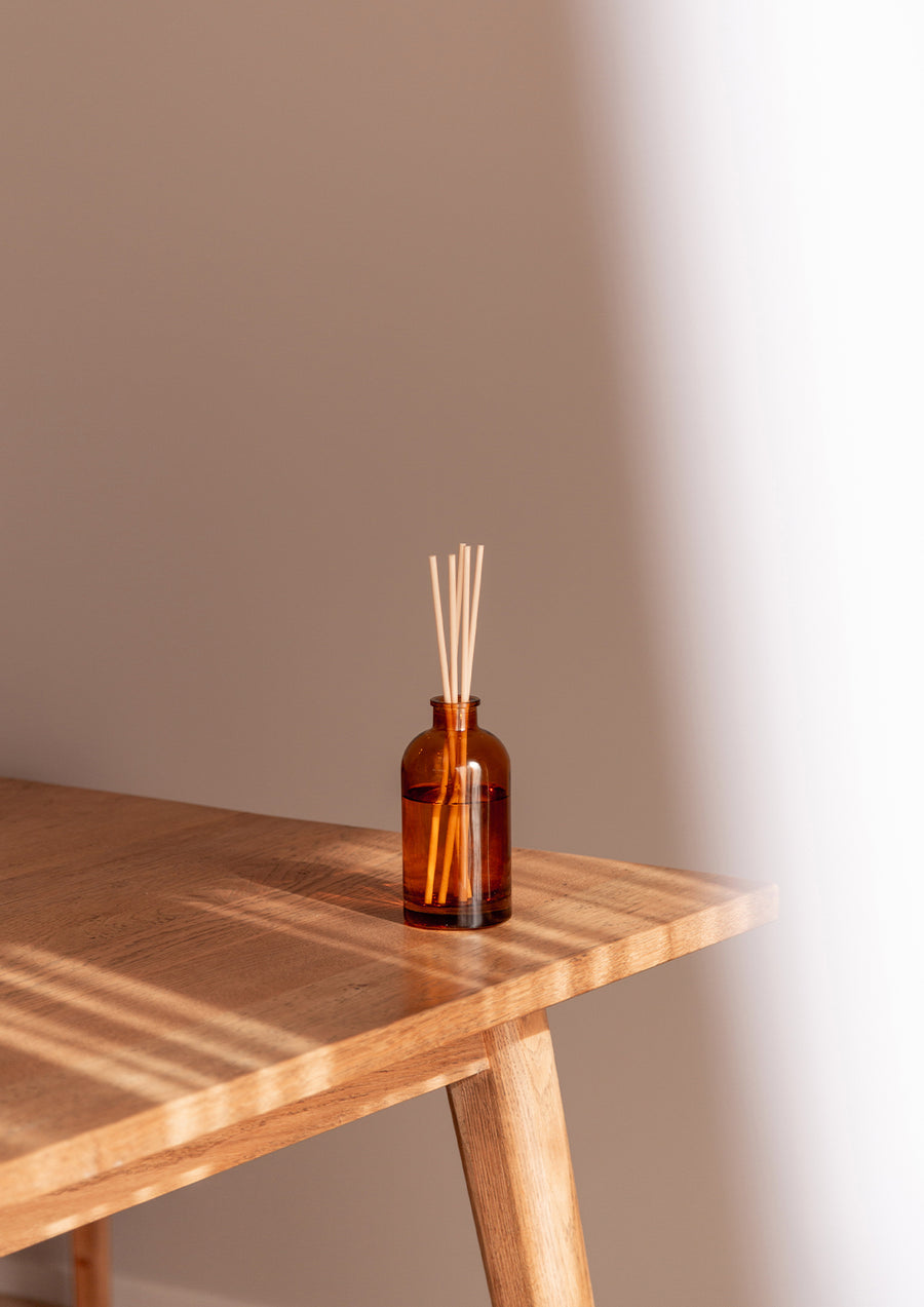 Therapy reed diffuser on the corner of a timber side table in soft shadow