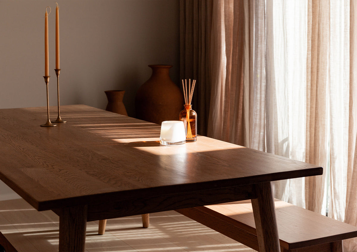 Therapy reed diffuser on a dark timber table beside a window