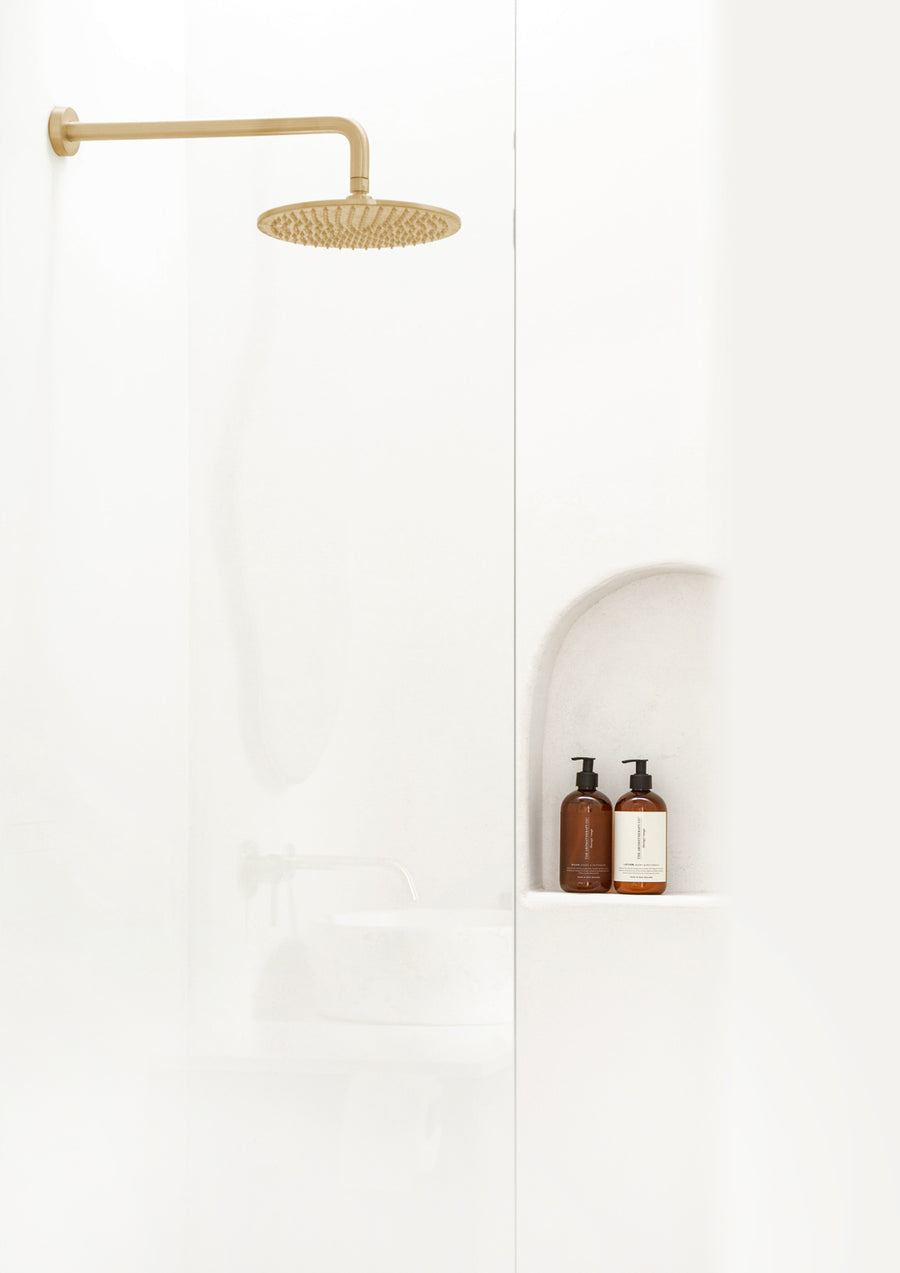 White walk-in shower with a brass rain head and two amber pump bottles in an arched niche