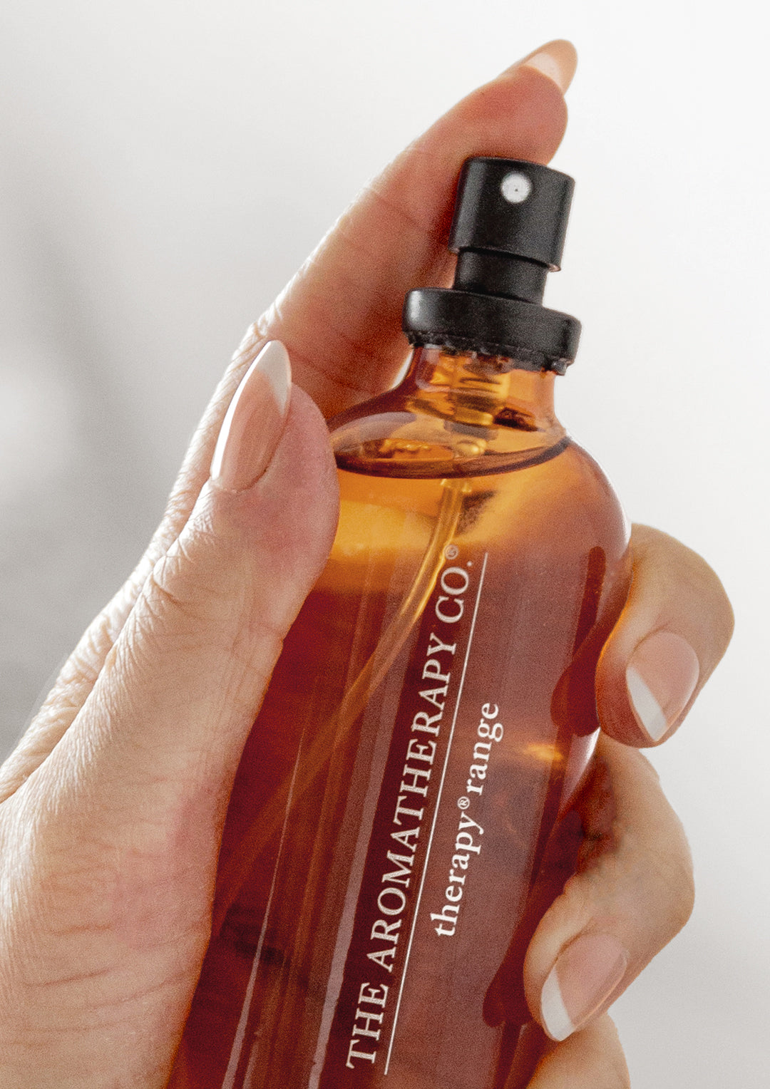 Close up of a hand pressing the black nozzle of an amber Therapy room spray