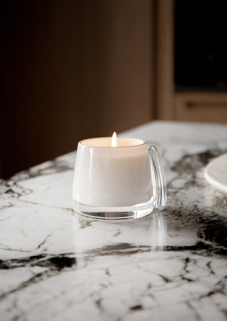 Lit Therapy candle on a marble benchtop with a blurred timber kitchen behind
