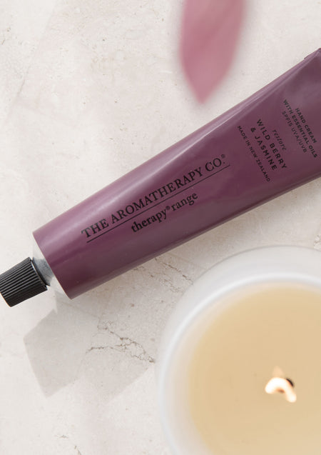 Close crop of the plum hand cream tube label beside a lit candle on marble